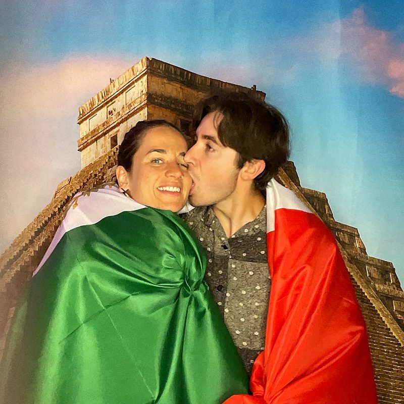 A couple wrapped in a flag, sharing a kiss on the cheek